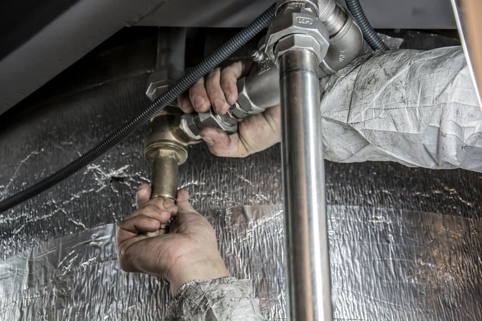 Hands fitting reflective insulation and piping beneath a floor in a crawl space