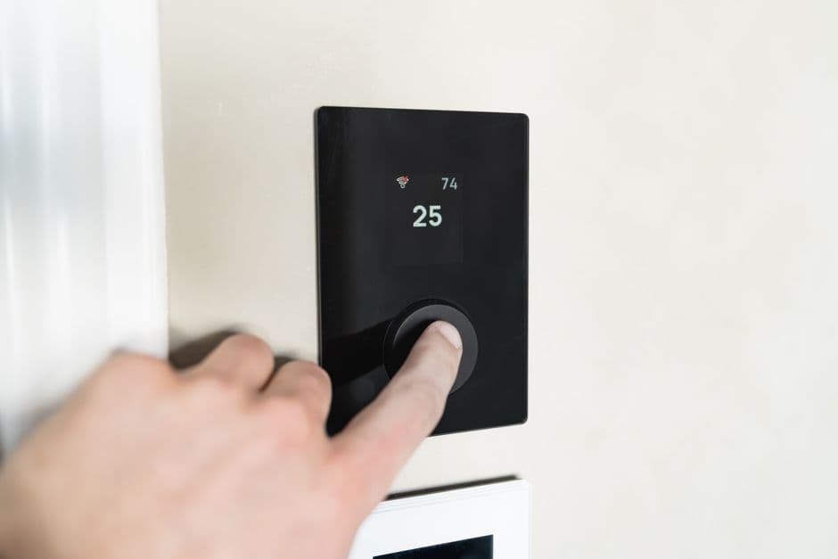 A hand adjusting a wall-mounted smart thermostat to lower the temperature