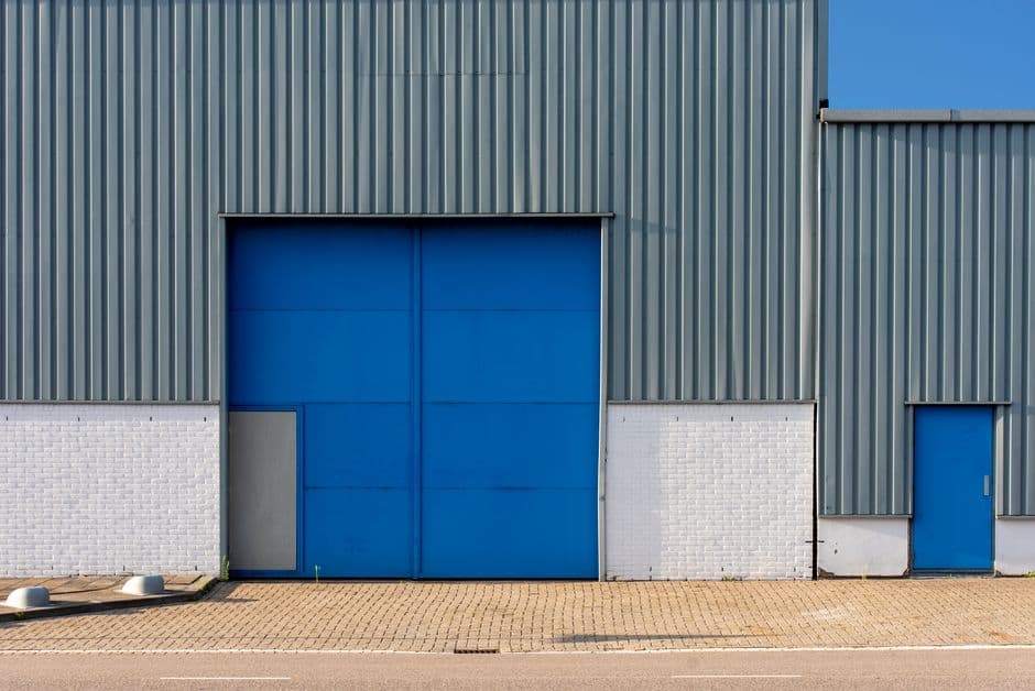 Exterior of a metal commercial warehouse building with a large blue loading door