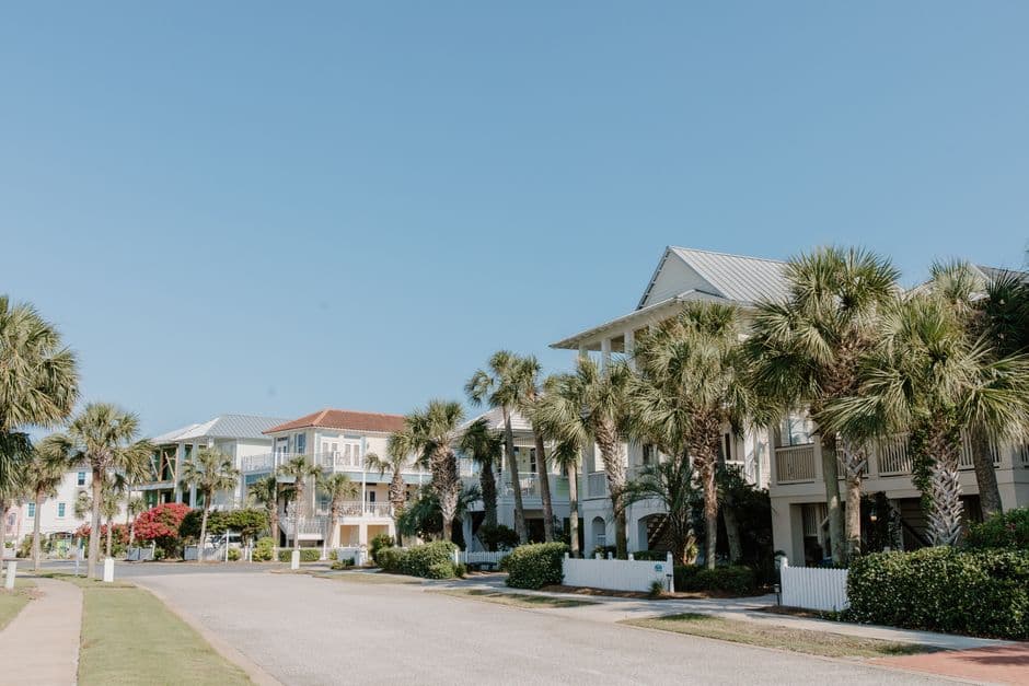 Row of elevated Gulf Coast homes lined with palm trees under a clear blue sky